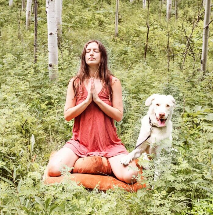 Vrouw mediteert in het bos met haar hond, rustgevende yogasessie in de natuur.